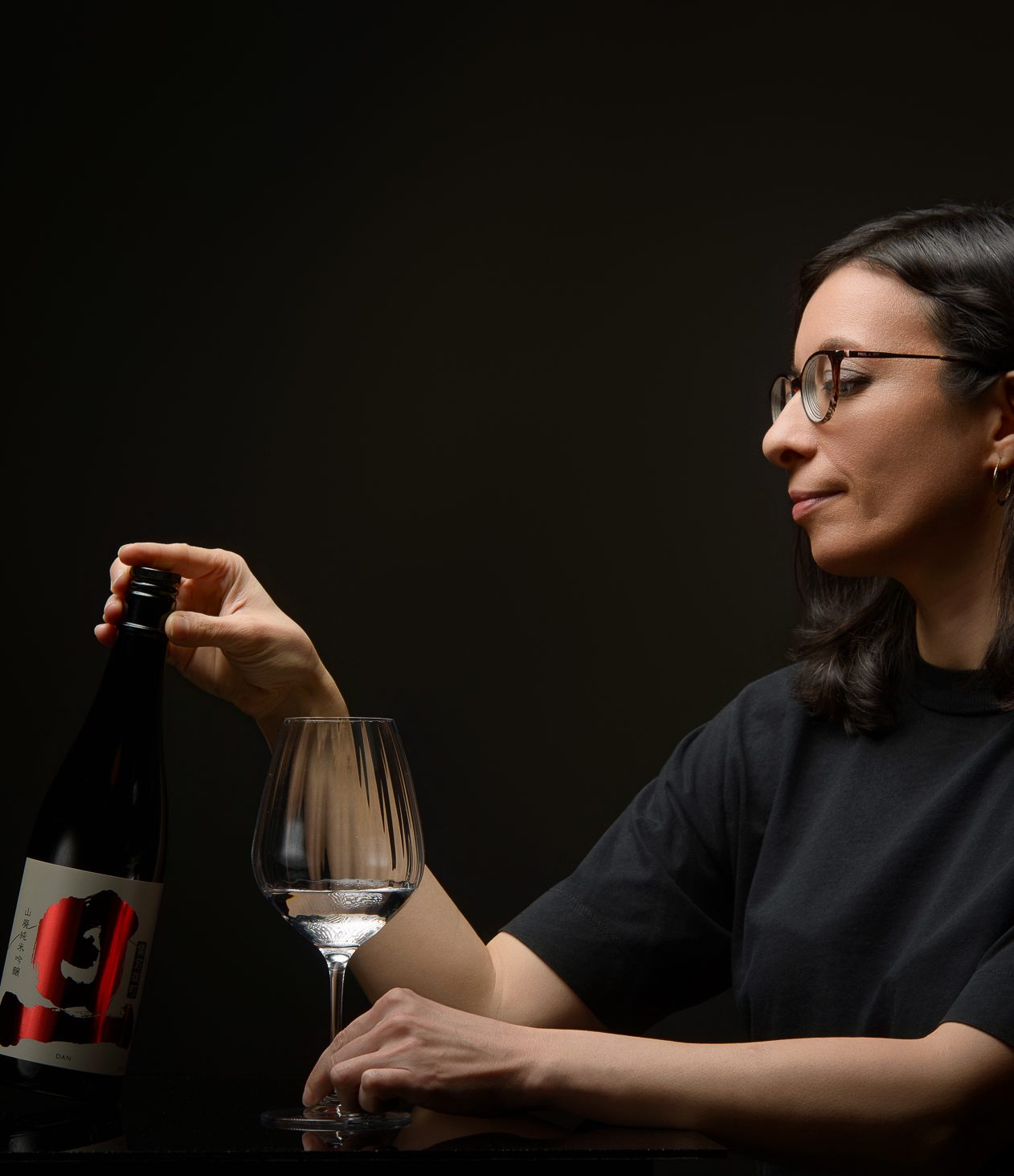 Karen, sommelière en saké, joue avec une bouteille prestigieuse de saké japonais et tient un verre de saké.